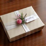 Ein festlich verpacktes Firmengeschenk, bestehend aus einem kleinen Blumenstrauß und einem polierten Edelstein